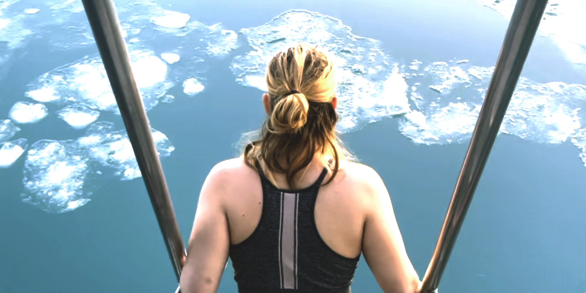 Jenn standing on the ladder of a ship, wearing a swimsuit, overlooking icebergs 